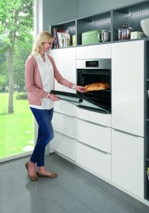 Frau entnimmt frisch gebackenes Brot aus einem modernen Einbaubackofen in einer weißen Küchenzeile